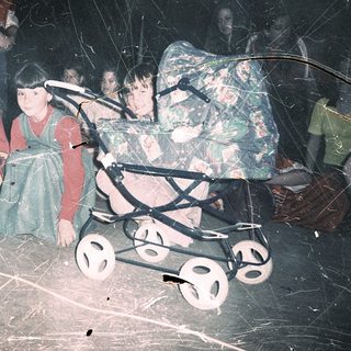 Displaced children in makeshift shelter with stroller.