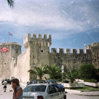 Medieval fortress by coastal promenade with flags.