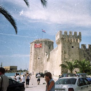 Medieval fortress by coastal promenade with flags.