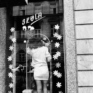 A person decorates a school window display with flower cutouts.