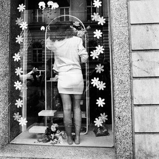 A person decorates a school window display with flower cutouts.