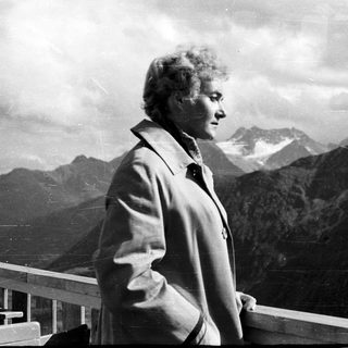 Woman standing by railing overlooking mountainous landscape.