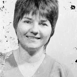 Short-haired woman smiling in vintage-style black-and-white photo.