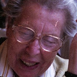 Elderly woman smiling by train window.