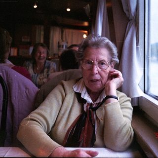 Elderly woman talking on phone inside train.
