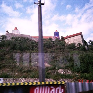 Castle ruins on hillside with modern buildings nearby.