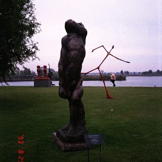 Bronze sculpture of a seated figure in park setting.