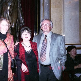 Three people posing indoors near statue.