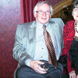 Two people smiling indoors at a cozy table.