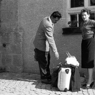 Couple standing with luggage outside building.