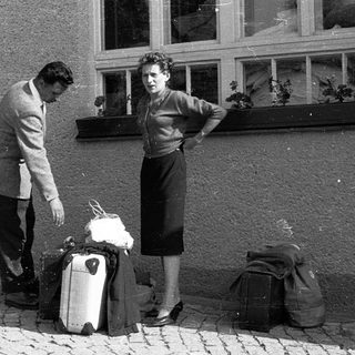 Couple standing with luggage outside building.