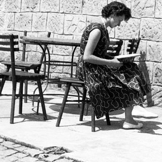 Woman reading outdoors at stone-walled café table.