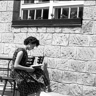 Woman reading outdoors at stone-walled café table.