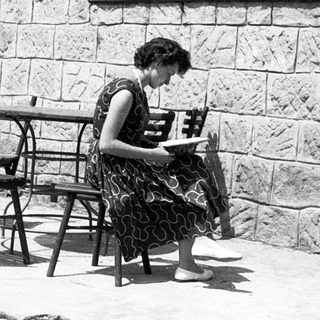 Woman reading outdoors at stone-walled café table.