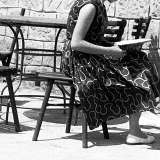 Woman reading outdoors at stone-walled café table.