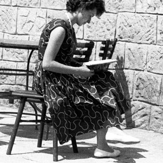 Woman reading outdoors at stone-walled café table.