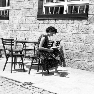 Woman reading outdoors at stone-walled café table.