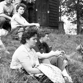Group of people relaxing outdoors near a wooden house.