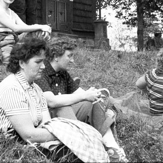 Group of people relaxing outdoors near a wooden house.