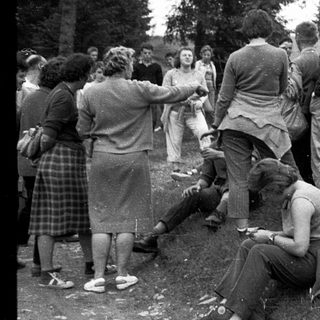 Group of people socializing outdoors in 1960s-style clothing.