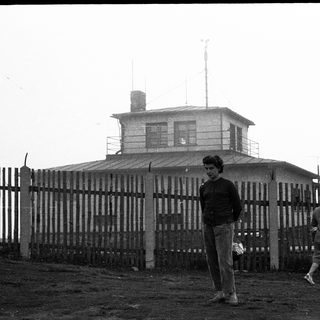 Two people near a watchtower with fenced area.