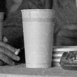 Two people sitting indoors, drinking from cups.