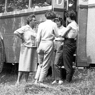 People gather near vintage buses in grassy area.