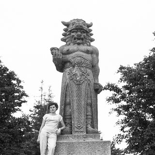 Woman posing beside Komainu guardian lion statue.