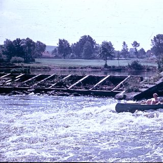 People rafting on turbulent river near dam.
