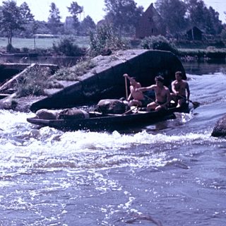 People rafting on turbulent river near dam.