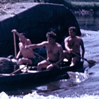 People rafting on turbulent river near dam.