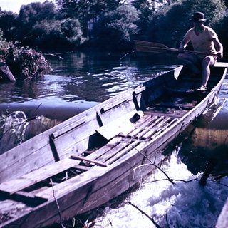 Man rowing wooden boat on river near dock.