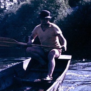 Man rowing wooden boat on river near dock.