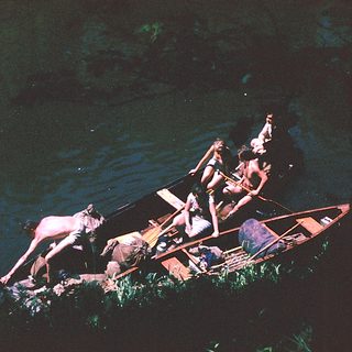 People rowing traditional wooden boat on water.