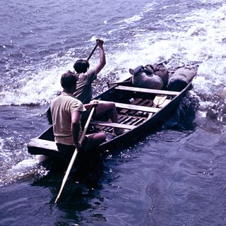 Boat being rowed through turbulent water near shore.