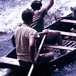 Boat being rowed through turbulent water near shore.