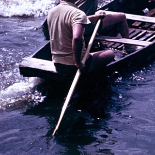 Boat being rowed through turbulent water near shore.