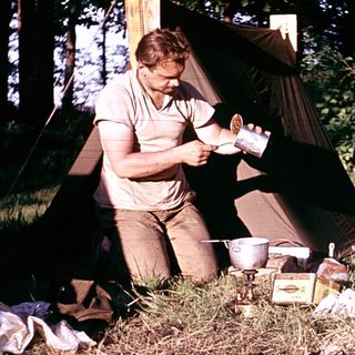 Man preparing food outdoors near camping tent.