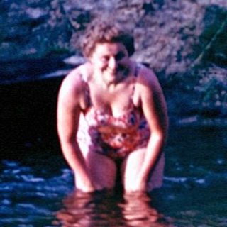 Person standing in shallow river near campsite.