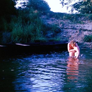 Person wading in shallow river near canoe.