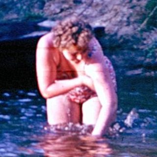 Person wading in shallow river near canoe.