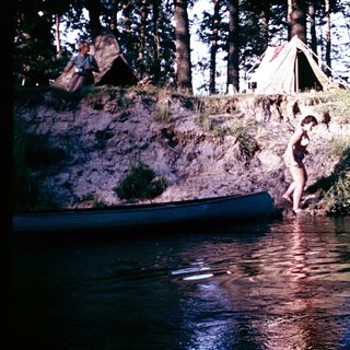 Campsite by water, person jumping into lake.