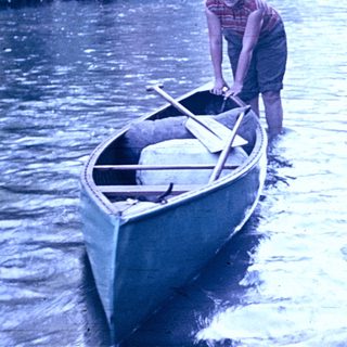 Man pushing canoe into calm river.