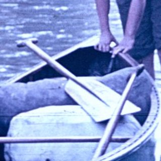 Man pushing canoe into calm river.