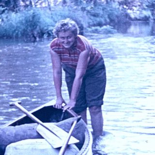 Man pushing canoe into calm river.
