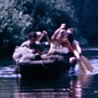 People canoeing on a calm river surrounded by greenery.