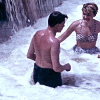 People swimming and playing under a waterfall.