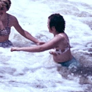 People swimming and playing under a waterfall.