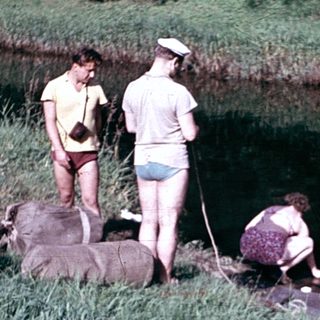 People preparing and launching a bamboo raft on riverbank.