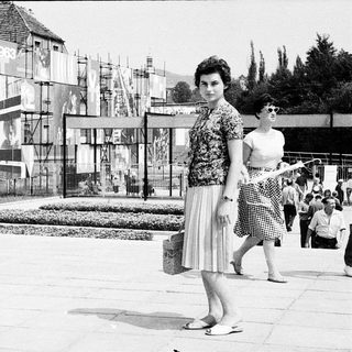 Mid-century outdoor event with modernist architecture and stylish 1960s attire.